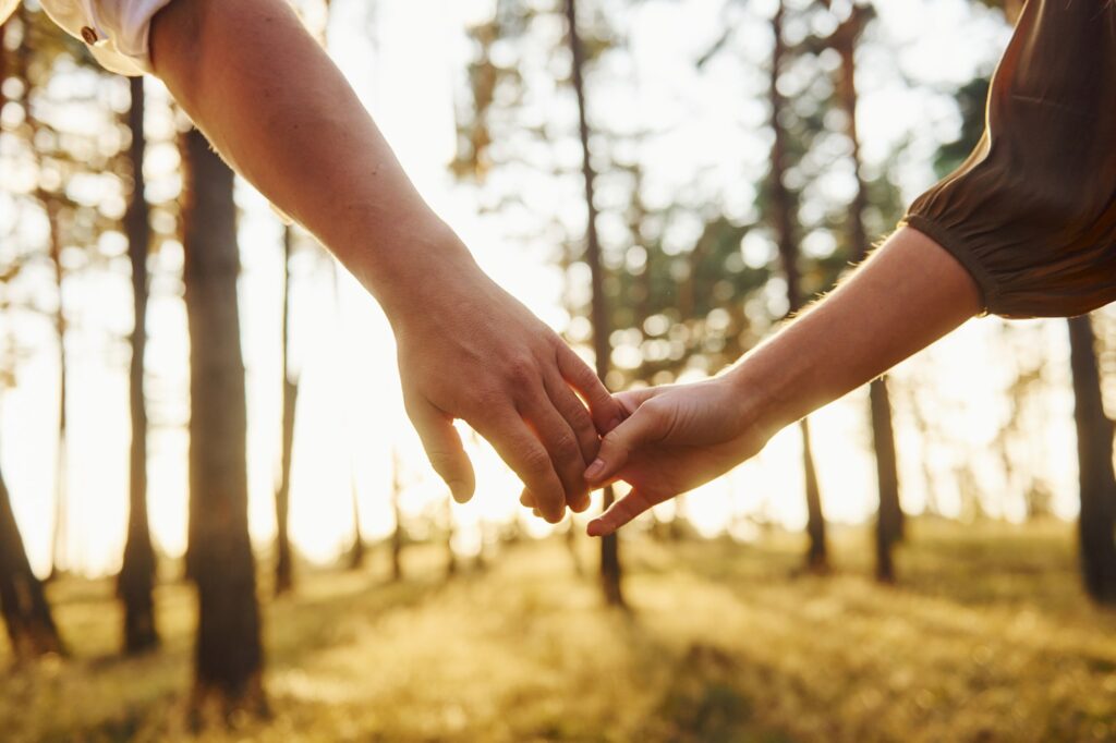 Close up view of hands. Happy couple is outdoors in the forest at daytime