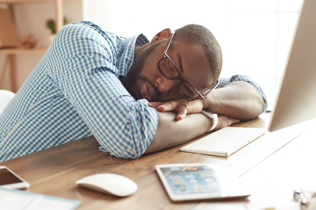 Taking a break. Tired afro american man in glasses sleeping at his working place at home. Afro