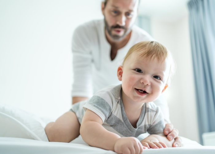 Caucasian parents play with cute baby boy child infant on bed at home.